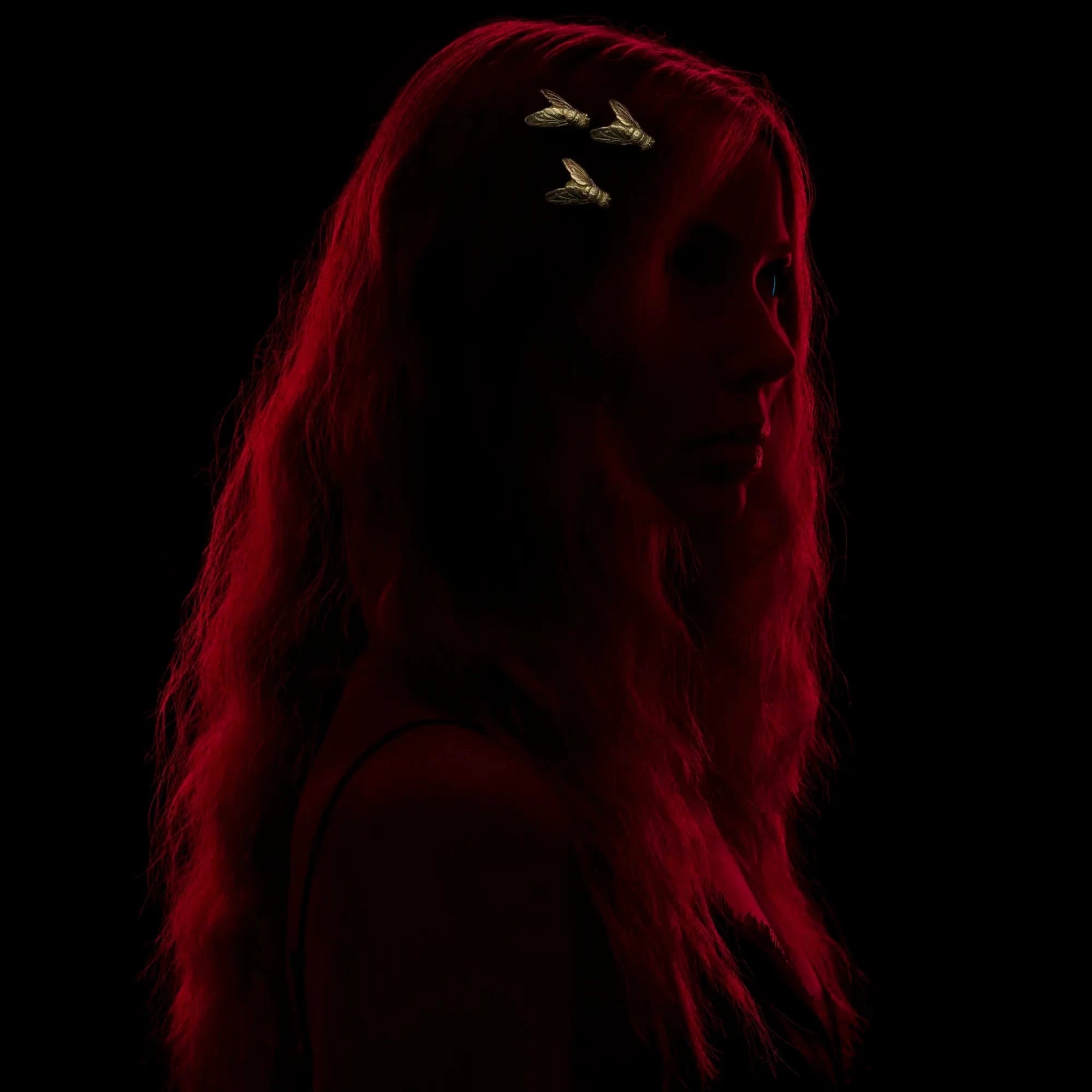 Model wears set of three gold blue bottle fly hair slides against a black background.