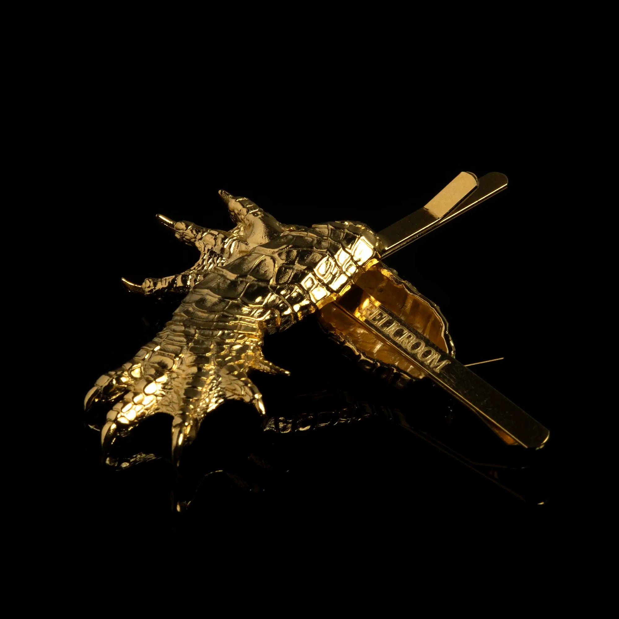 A pair of Gold Alligator Claw Hair Slides with Relic Room logo on the bottom of the hair slide against a black background.