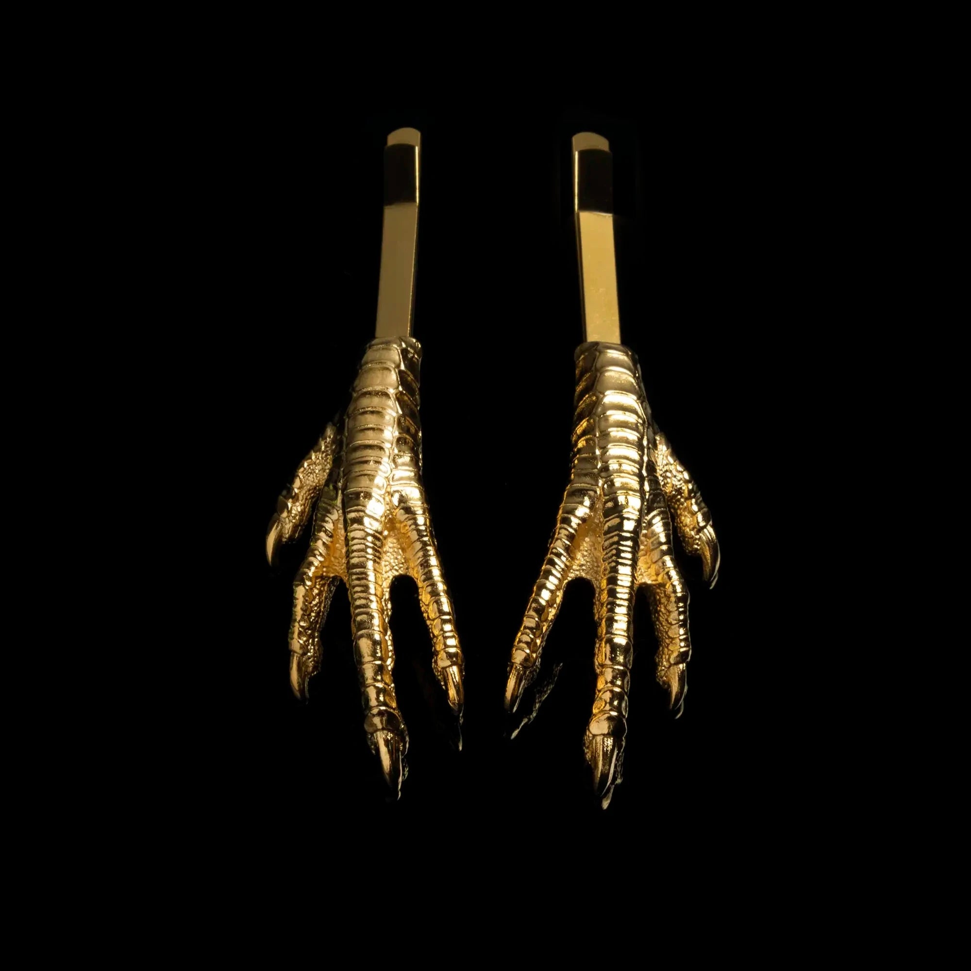 A set of two mirrored gold chicken feet hair slides against a black background. 
